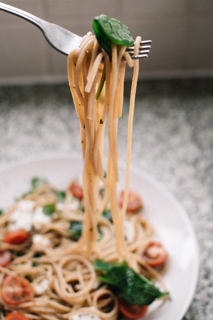 about-us Close-up of freshly cooked spaghetti with cherry tomatoes, spinach, and mozzarella cheese on a plate.