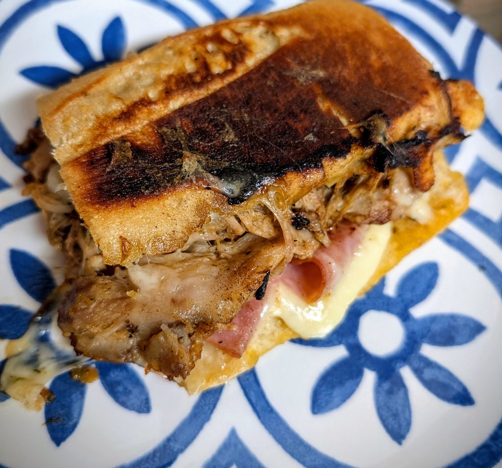 Cuban-style pernil sandwich with melted Swiss cheese, ham, pickles, and crispy pressed bread